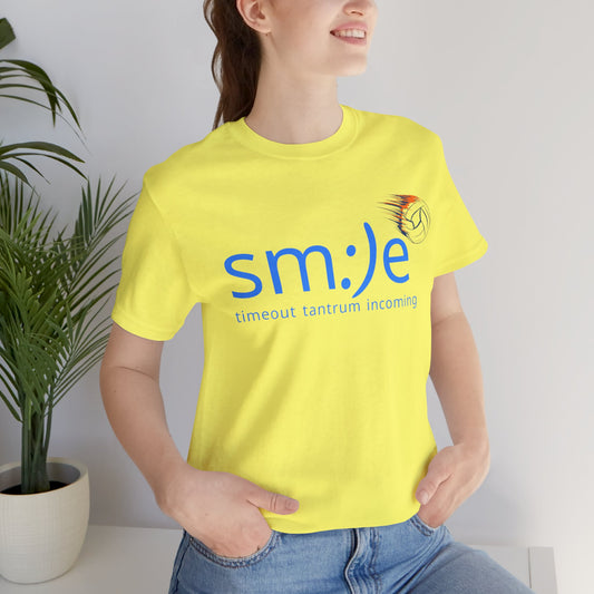 Person indoors beside a plant, wearing a yellow volleyball-themed shirt with a smiley face and the text “sm:)e Timeout tantrum coming.”