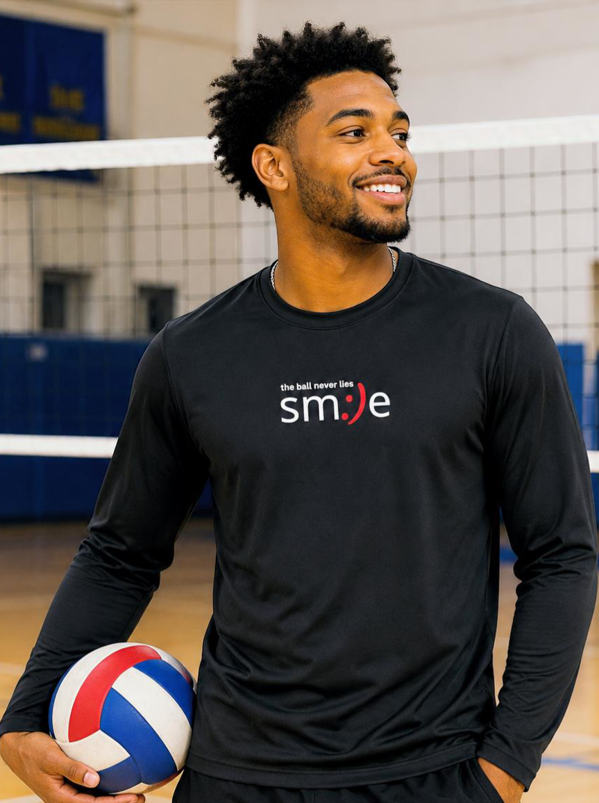 Man holding a volleyball in an indoor sports facility wearing a black shirt with text.