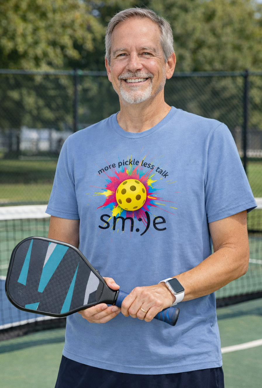 Man holding a pickleball paddle on a court wearing a blue t-shirt with a pickleball design.